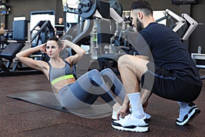 Trainer helping young woman to do abdominal exercises in gym