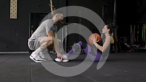 Trainer helping young woman to do abdominal exercises in gym slow motion.