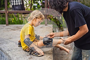 Trainer helps the boy to wear knee pads and armbands before training skate board