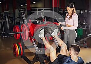Trainer with man working out on leg press machine