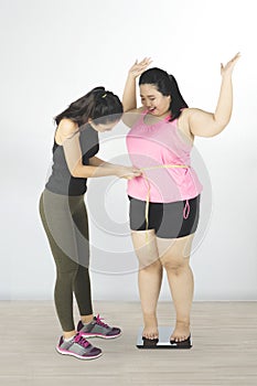 Trainer measuring belly of fat woman