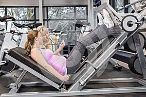 Trainer motivating pregnant woman while using leg press