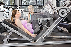 Trainer motivating pregnant woman while using leg press