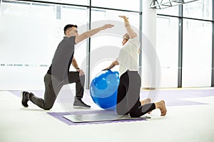 Trainer show exercise with ball to a senior woman