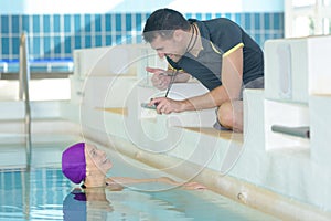 Trainer showing cronometer at swimmer at pool