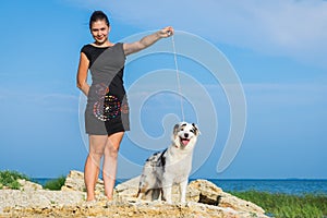 The trainer training with the dog australian shepherd team stand on the against a blue sky on a stony beach