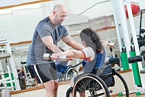 Trainer with woman in wheelchair lifting weight in gym. sport activity of people with disability