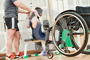 Trainer with woman in wheelchair lifting weight in gym. well being of disabled people