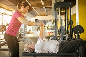 Trainer working exercise with senior woman in the gym.