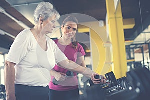 Trainer working exercise with senior woman in the gym.