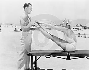Trainer and young woman doing exercises at the beach