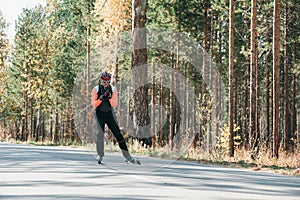 Training an athlete on the roller skaters. Biathlon ride on the roller skis with ski poles, in the helmet. Autumn photo