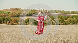 Training in the autumn field - a belligerent woman in red traditional dress wields with a sword