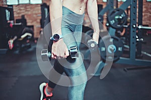 Training concept. Closeup of tense leg muscles in leggings.Fitness woman with sports body exercising with dumbbells in the gym.