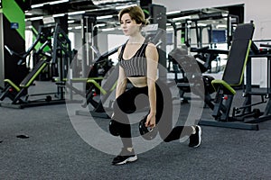 Training legs in the gym. Attractive fit Caucasian woman doing lunges with discs from the bar.