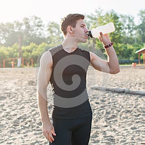 Training Outdoors. Athletic fit man drinking water after running workout at beach.