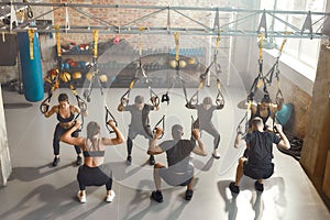 The Training Space. Group of sportive people doing fitness TRX training exercises at industrial gym. Push-up, group