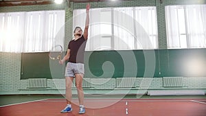 Training on the tennis court. Young man catch the ball from the floor and innings it