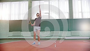 Training on the tennis court. Young man throws the ball in the air and innings it