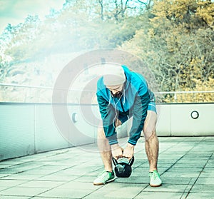 Training on the terrace of the house, overlooking the forest, young man with a beard lifts weights