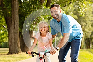 Training wheels and tender moments. Adorable girl learning to ride a bicycle with her father outdoors