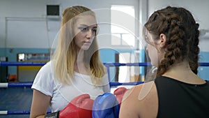 Training, young sports girls in boxing gloves angrily look each other in eye before fight in the ring at gym