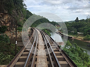 A trainrail in Asia, running along a river with boats lined up along the riverbed