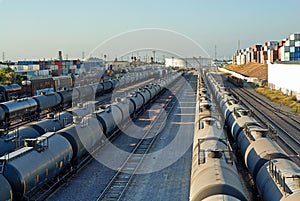 Trains carrying fluids merge at the point of a large fuel storage tank.