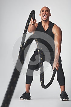 He trains insane. Studio shot of an athletic young man working out with battle ropes against a grey background.
