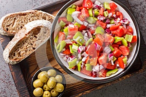 Trampo ensalada salad made with tomatoes, peppers, and onions served with olive and bread closeup on the wooden board. Horizontal photo