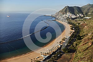 Tranquil beach curves along a coastal town with mountains in the background, captured at sunrise