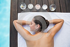 Tranquil brunette lying on towel poolside with beauty treatments