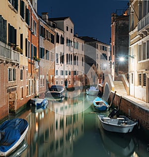 Tranquil canal with colorful buildings and boats at night, Venice, Italy