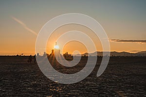 Tranquil desert sunset at art festival with silhouetted structure, attendees, and mountains