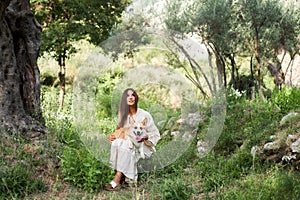 A tranquil embrace in nature: a woman cradles a corgi in a serene olive grove