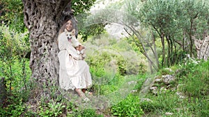 A tranquil embrace in nature: a woman cradles a corgi in a serene olive grove