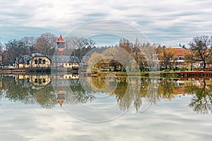 Tranquil landscape with lake, houses, cloudy sky, and trees reflected symmetrically in the water. Nyiregyhaza, Hungary