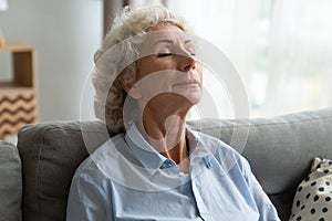 Tranquil middle aged senior female retiree relaxing on comfortable sofa.