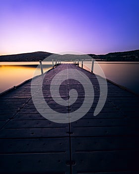Tranquil pier extending out into a tranquil lake with a breathtaking sunset in the background.