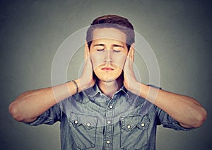 Tranquil, relaxed young man covering ears, eyes closed