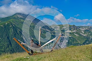 Tranquil Retreat: Man in Black Apparel Resting in Hammock Amidst Lush Mountain and Azure Sky Scenery