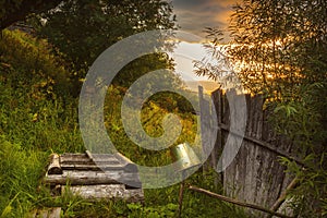 Tranquil rural landscape with old well and bucket on the hill against the sunset.