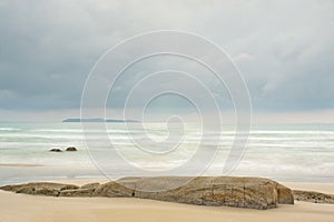 Tranquil scene of a beach at the sea with an island in the background and rocks in the foreground