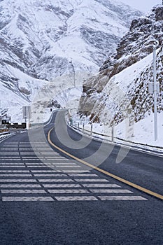 Tranquil scene of an empty road in the foreground, with rugged snowy mountains in the distance