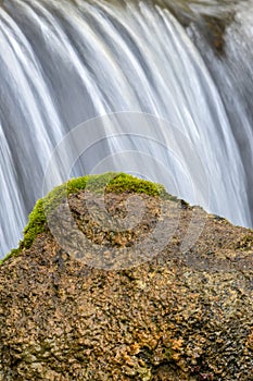 Tranquil scene of nature in the woods featuring a moss-covered rock with a waterfall cascading over