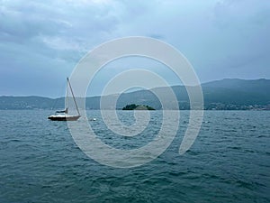 Tranquil Scene of a Sailboat Moored in Lake Maggiore with Isola Madre in the Distant Misty Background, Verbania, Italy