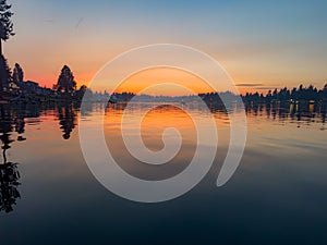 Tranquil scene of a sunset, with silhouetted trees and still water reflecting the sky's warm hues