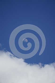 Tranquil scenery of the moon above the puffy cumulus clouds on the blue sky