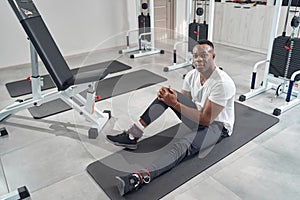 Tranquil sportsman posing for camera among gym equipment