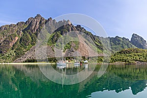 A tranquil summer scene in the Lofoten Islands, where sailboats and traditional Rorbu cabins are mirrored in the still water